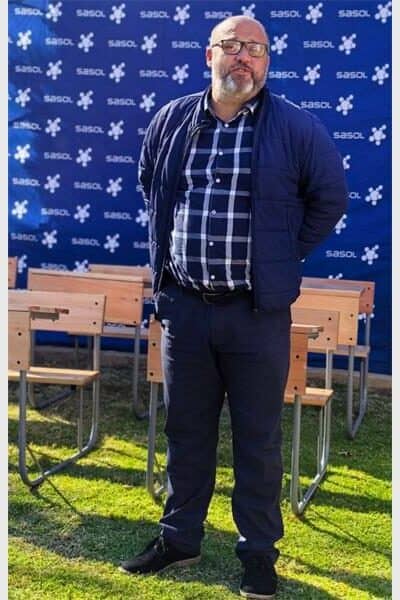 man with beerd stands with desks in front of a Sasol backdrop