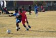 soccer players in blue and one in pink vie for the ball