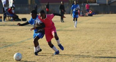 soccer players in blue and one in pink vie for the ball