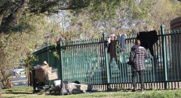 a vagrant hanging up washing over a palisade fence in the central business district