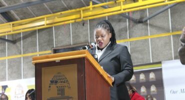 a woman in a suit standing behind a podium speaking over a microphone
