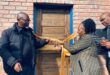 Three people at the ribbon cutting in front of a door