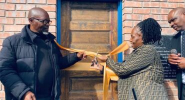 Three people at the ribbon cutting in front of a door