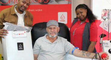 a blood donor is flanked by two employees of the blood bank