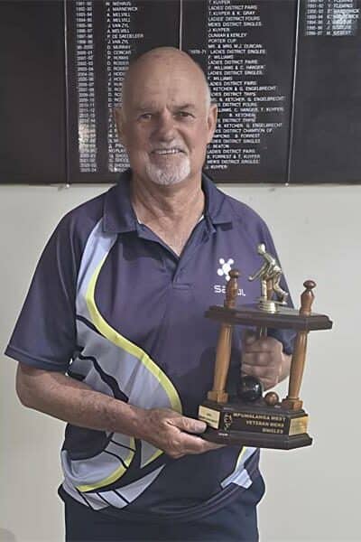 elderly man in blue sports wear holds up a trophy