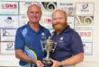 Two men in blue and white sport clothes hold up a trophy