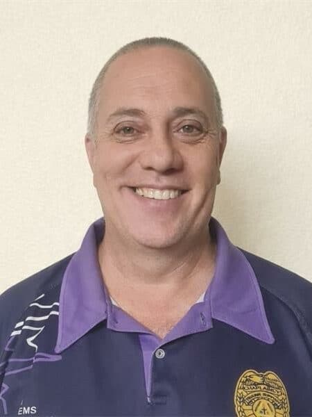 Close-up image of a bald man wearing a purple shirt, against a plain white background.