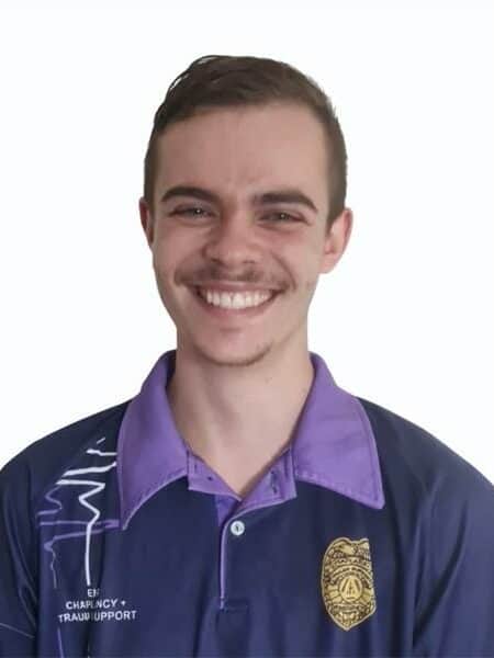 Close-up image of a young man with short brown hair, wearing a purple shirt, against a plain white background.