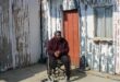 man in a wheelchair in front of a shack