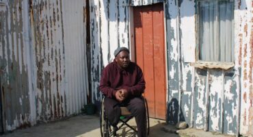 man in a wheelchair in front of a shack