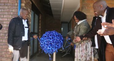 three people cutting a blue ribbon