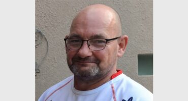 man with bold head, spectacles and a rugby shirt