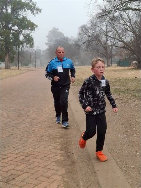 a boy runs on a dirt road, followed by an older man
