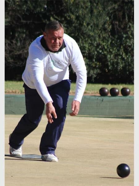 man in a white jersey and black trousers plays bowls