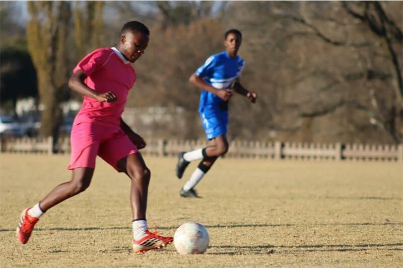 soccer players in blue and one in pink vie for the ball