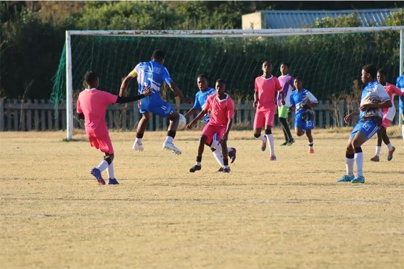 soccer players in blue and one in pink vie for the ball