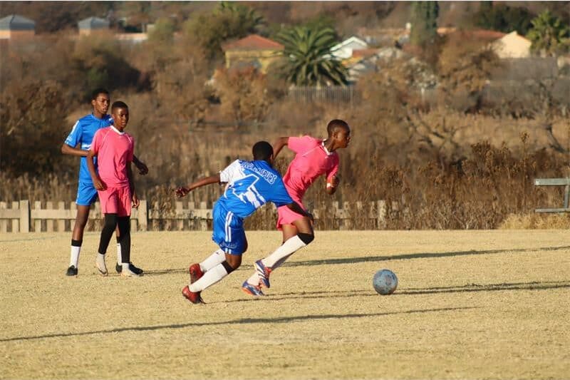 soccer players in blue and one in pink vie for the ball