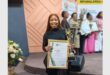 woman in a black outfit holds up a certificate