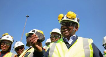 man in a reflector jacket and hard hat inspects a lump of coal.
