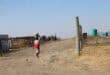 a woman carries a bucket of water on her head along a dirt road