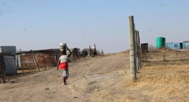 a woman carries a bucket of water on her head along a dirt road