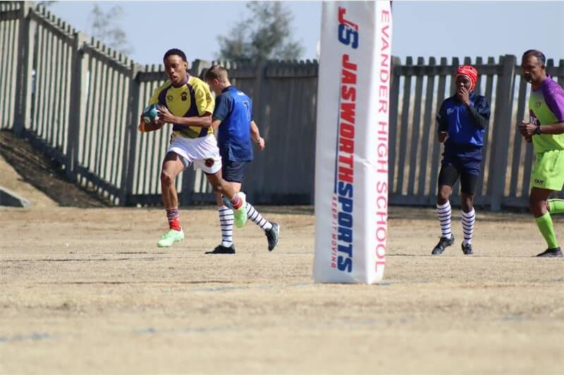 a boy in a yellow rugby jersey runs behind the poles