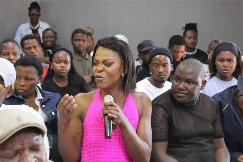 A transgender person in a pink top speaks over a microphone