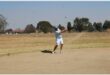 man in a light blue shirt plays golf out of a bunker