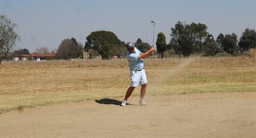 man in a light blue shirt plays golf out of a bunker