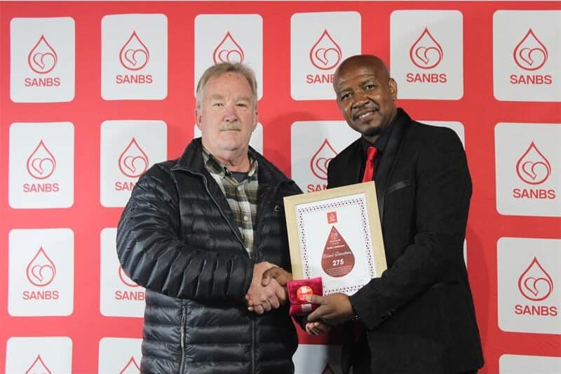 Two men hold up a certificate. The red background contains logos of the SANBS