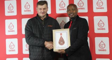 Two men hold up a certificate. The red background contains logos of the SANBS