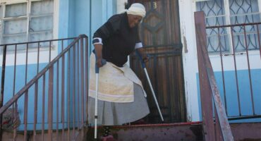 old woman with crutches at the top of a flight of stairs