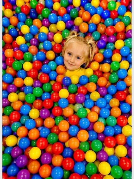 Young girl playing in a vibrant ball pit with multicoloured balls.