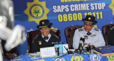 two police women sit in front of a police banner