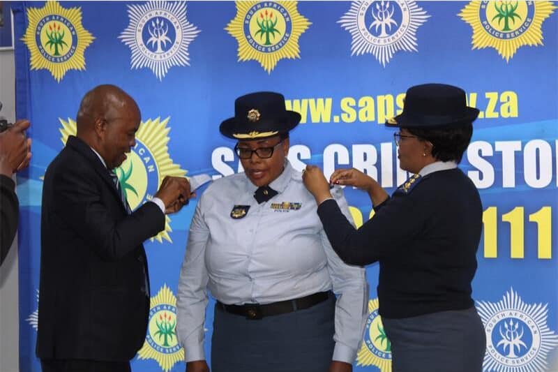 Two people in police uniform pin rank pins onto a police woman's epaulettes