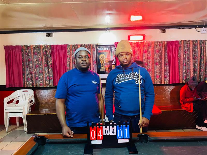 two men in blue shirts standing at a pool table