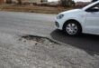 a big pothole and a white vehicle is driving past it