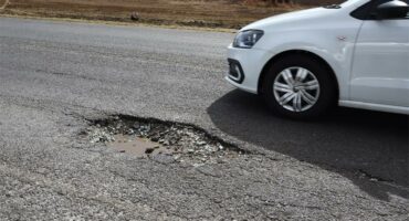 a big pothole and a white vehicle is driving past it