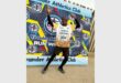 A man in athletics clothes poses in front of a colourful wall