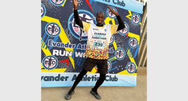 A man in athletics clothes poses in front of a colourful wall