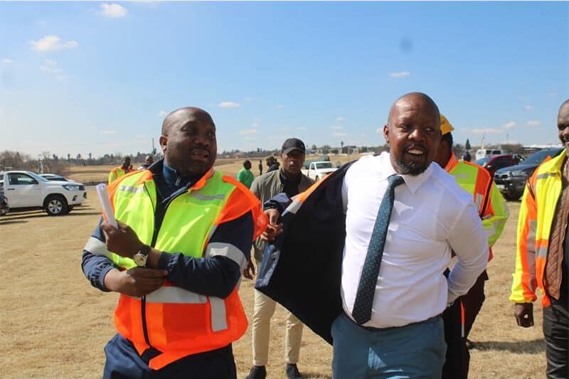 A man in a reflector jacket talk to another in a suit and tie