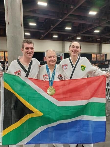 three people in karate outfits hold up the SA flag