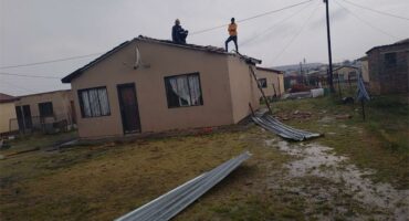 people stand on top of a house of which the roof had blown off