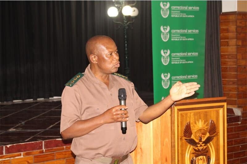 a man in correctional services uniform speaks over a microphone.