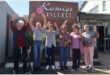 old people with hands in the air in front of a building named Kosmos Village