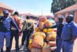 police with a huge load of bags. two men are hand cuffed in the background