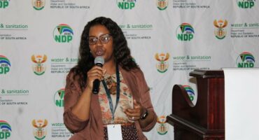 woman with a microphone. The backdrop is the the government and the department water and sanitation