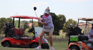 Woman with a white cap whacks the ball. There are golf carts in the background